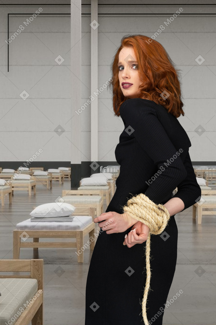 Tied up woman standing in a room with beds