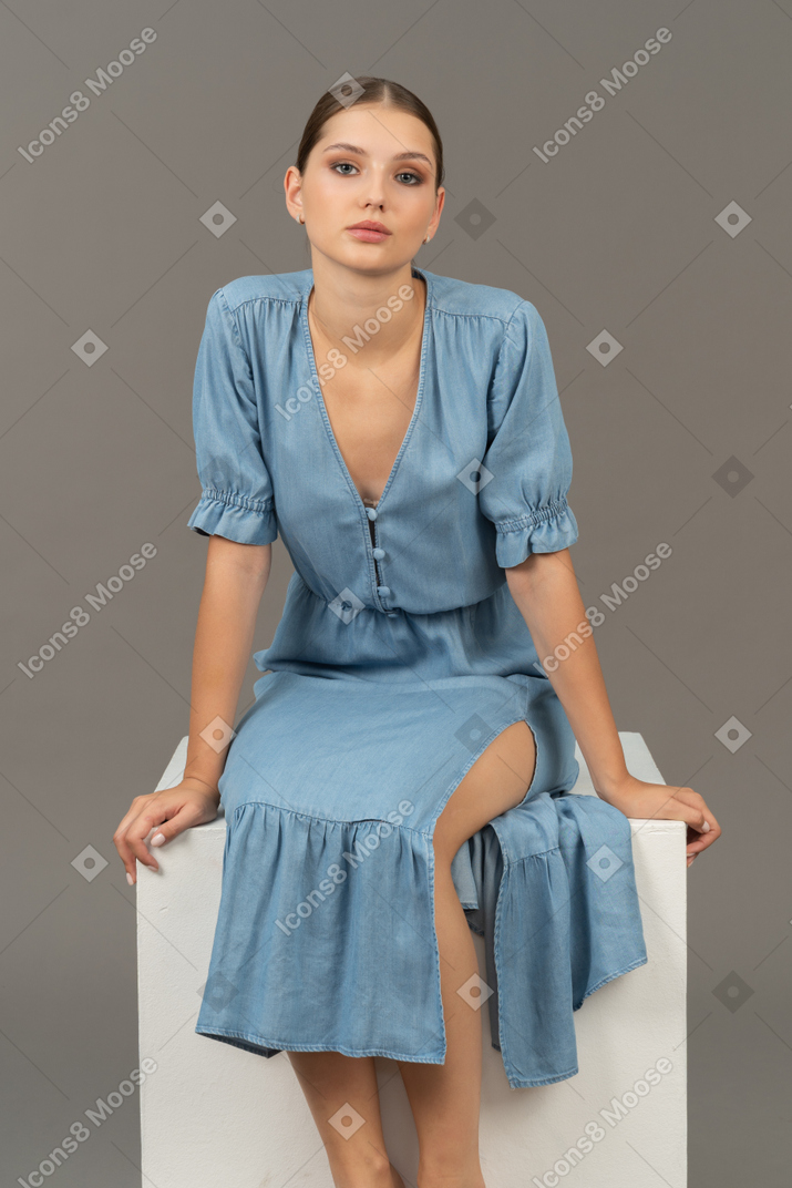Front view of young woman sitting on a cube and looking at camera