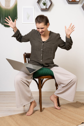 Front view of an irritated young woman with a headache sitting on a chair with a laptop