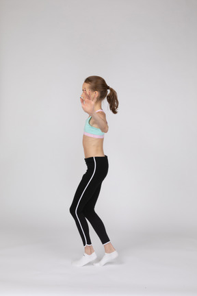 Vista laterale di una ragazza adolescente in abiti sportivi in equilibrio sulla punta dei piedi mentre si alzano le mani