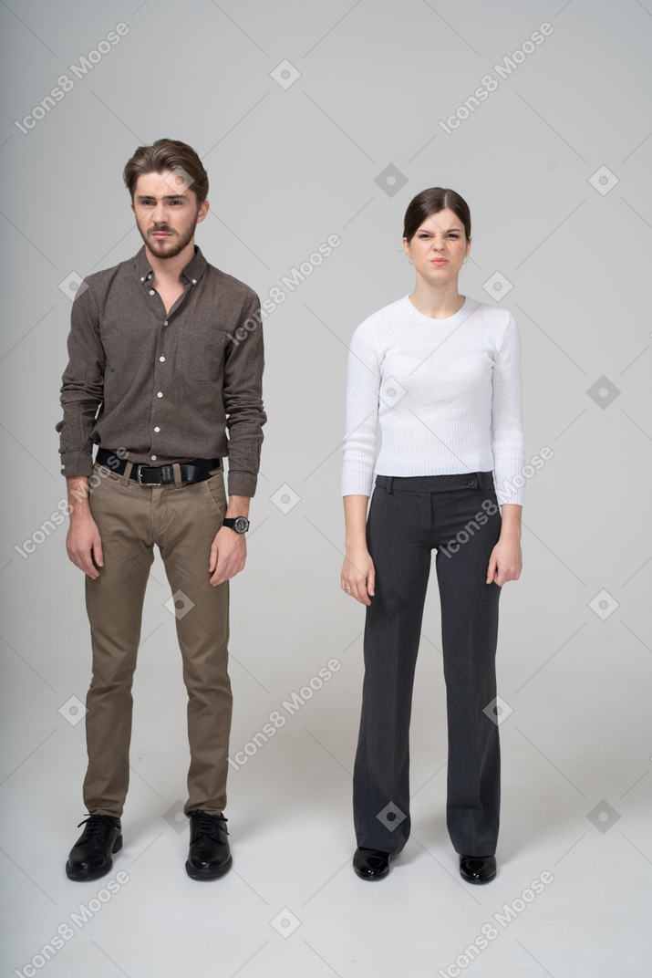 Vista frontal de um jovem casal descontente com roupas de escritório tricotando sobrancelhas