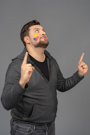 Three-quarter view of a male football fan with colorful face art raising fingers