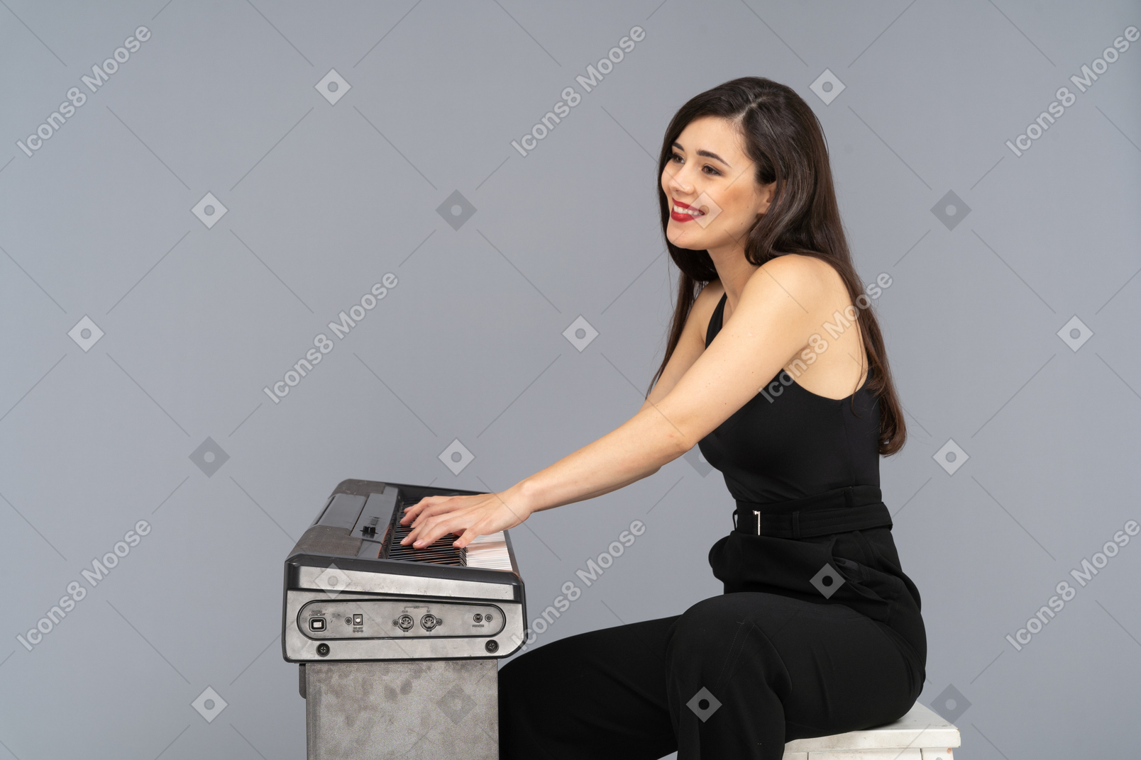 Vista lateral de una joven sentada sonriente en traje negro mientras toca el piano