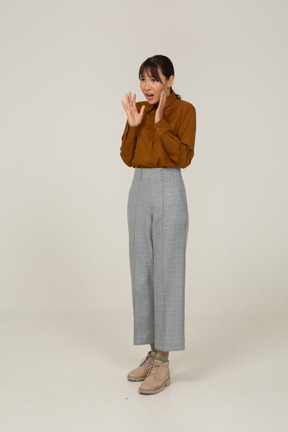 Three-quarter view of a shocked young asian female in breeches and blouse raising hands