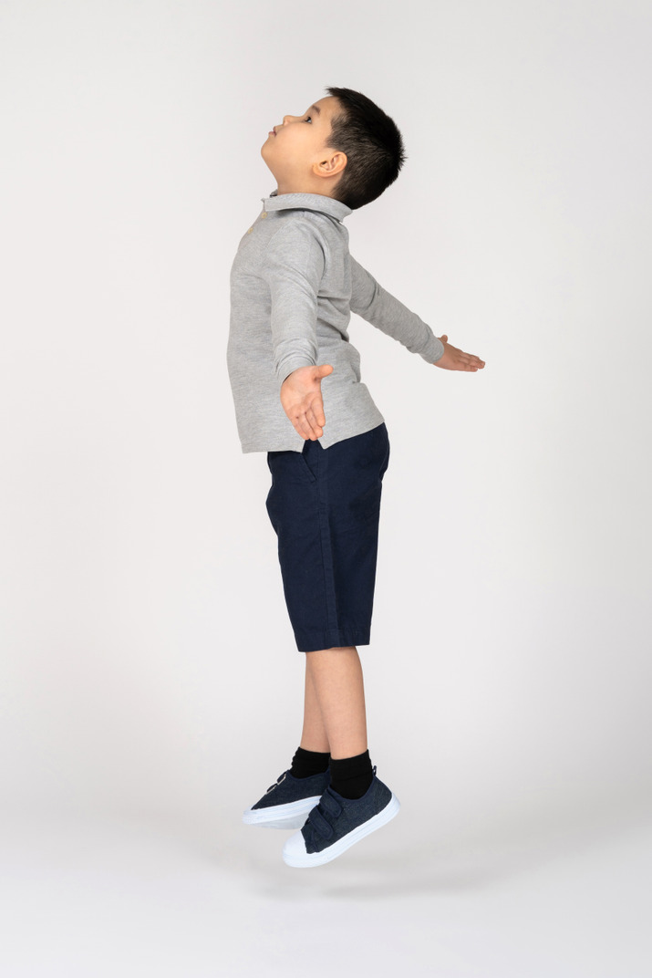 Boy jumping with spread arms in profile