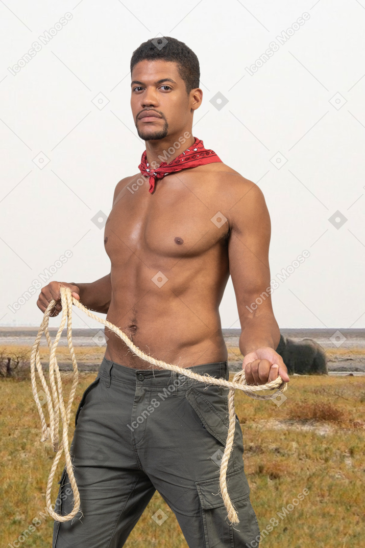 A shirtless man holding a rope in a field