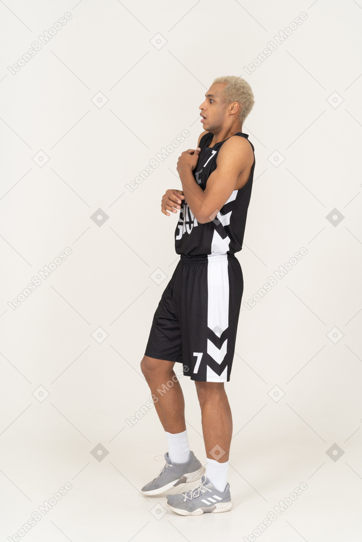 Vista laterale di un giovane giocatore di basket maschio sorpreso che tocca lo stomaco
