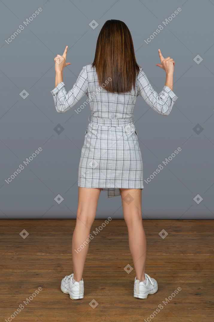 Mulher magro, de pé para a câmera e apontando para cima com dois dedos