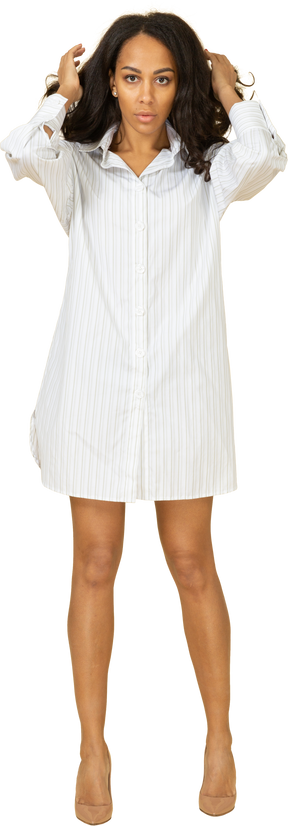 Vue de face d'une jeune femme à la peau foncée en robe blanche fixant ses cheveux