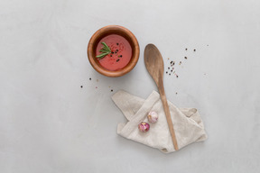 A bowl of gazpacho, some garlic and wooden spoon