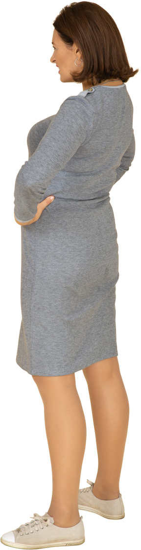 Vista laterale di una donna in abito grigio in piedi con le mani sui fianchi