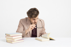 Apuesto joven sosteniendo sus gafas y leyendo un libro