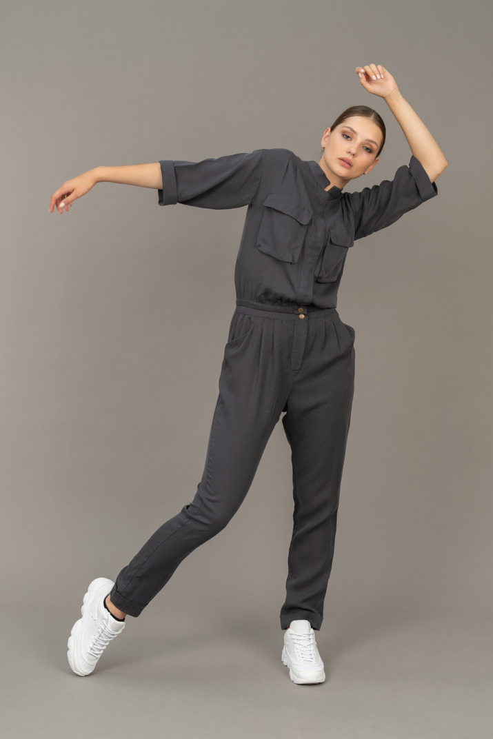 Front view of a dancing young woman in a jumpsuit raising hand