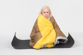 Mature woman sitting on yoga mat wrapped in blanket