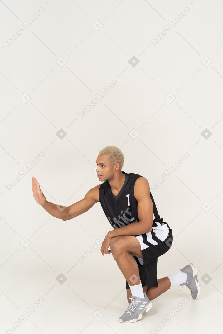 Vista de tres cuartos de un joven jugador de baloncesto masculino sentado dando un choca los cinco