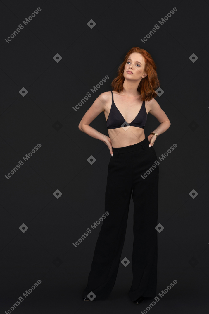 A frontal view of the beautiful woman dressed in black clothes holding her hands on the belt and posing