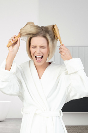 Woman combing her hair with a brush and screaming