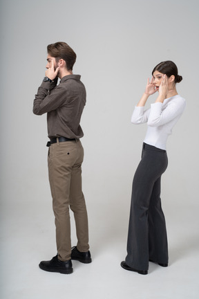 Vista lateral de um jovem casal surpreso com roupas de escritório tocando o rosto