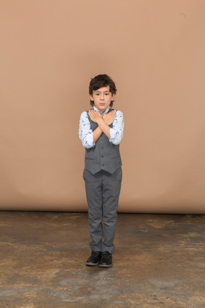 Vista frontal de un chico lindo en traje de pie con las manos en los hombros