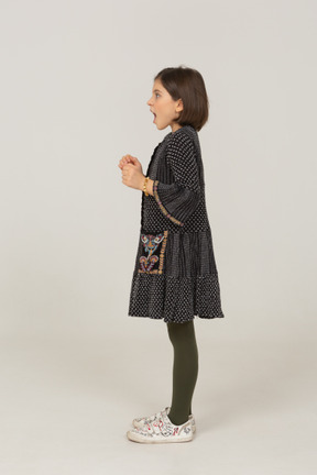 Vista lateral de una niña emocionada con vestido apretando los puños