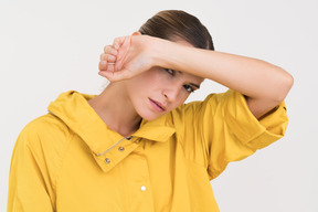 Femme en anorak jaune fermant son visage avec une main