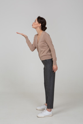 Vista lateral de una señorita en jersey y pantalones enviando un beso al aire
