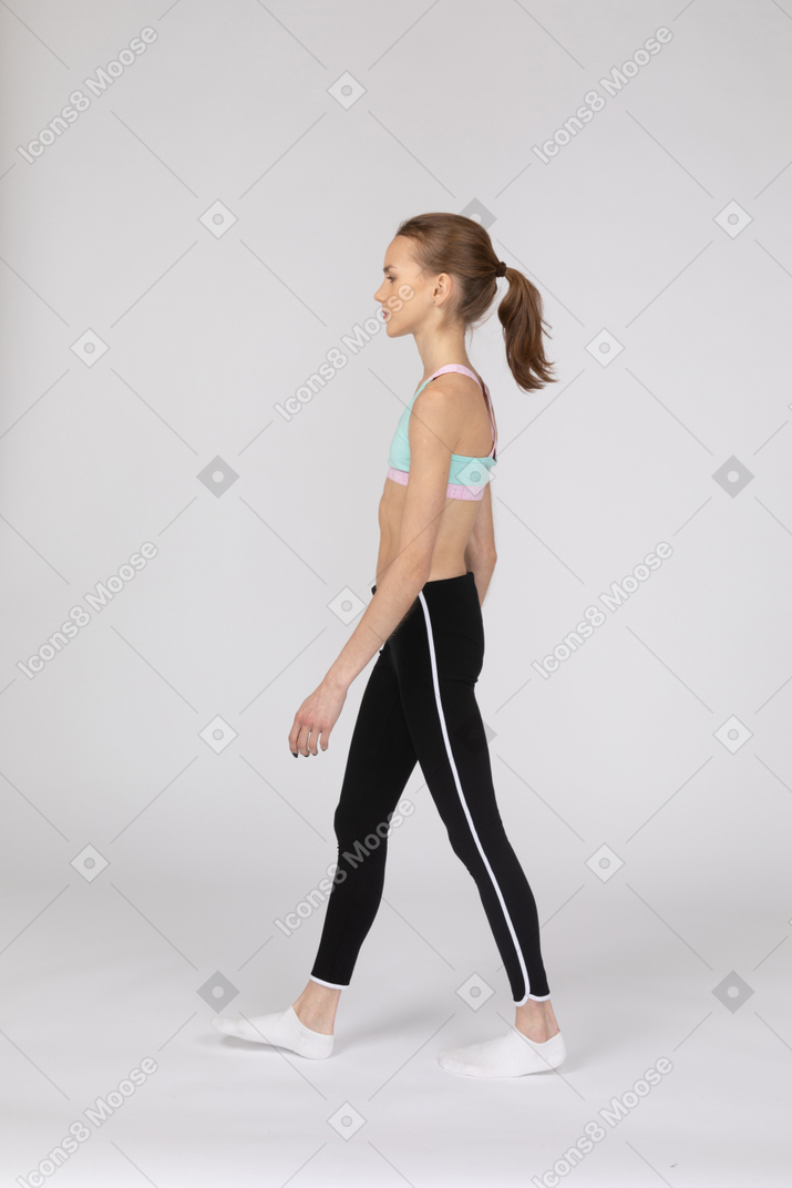 Vista lateral de uma adolescente em roupas esportivas caminhando