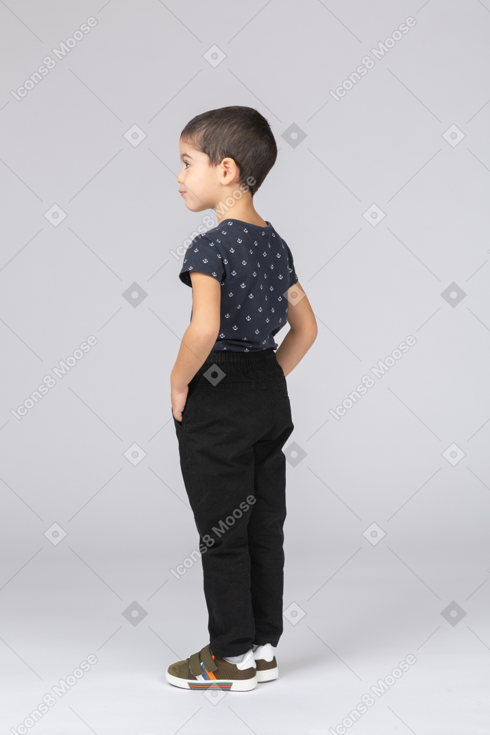 Side view of a cute boy in casual clothes standing with hands in pockets