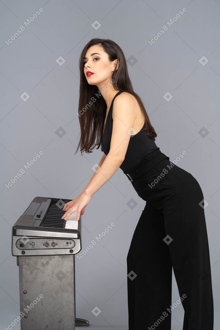 Vista lateral de uma jovem de terno preto tocando piano enquanto levanta a cabeça