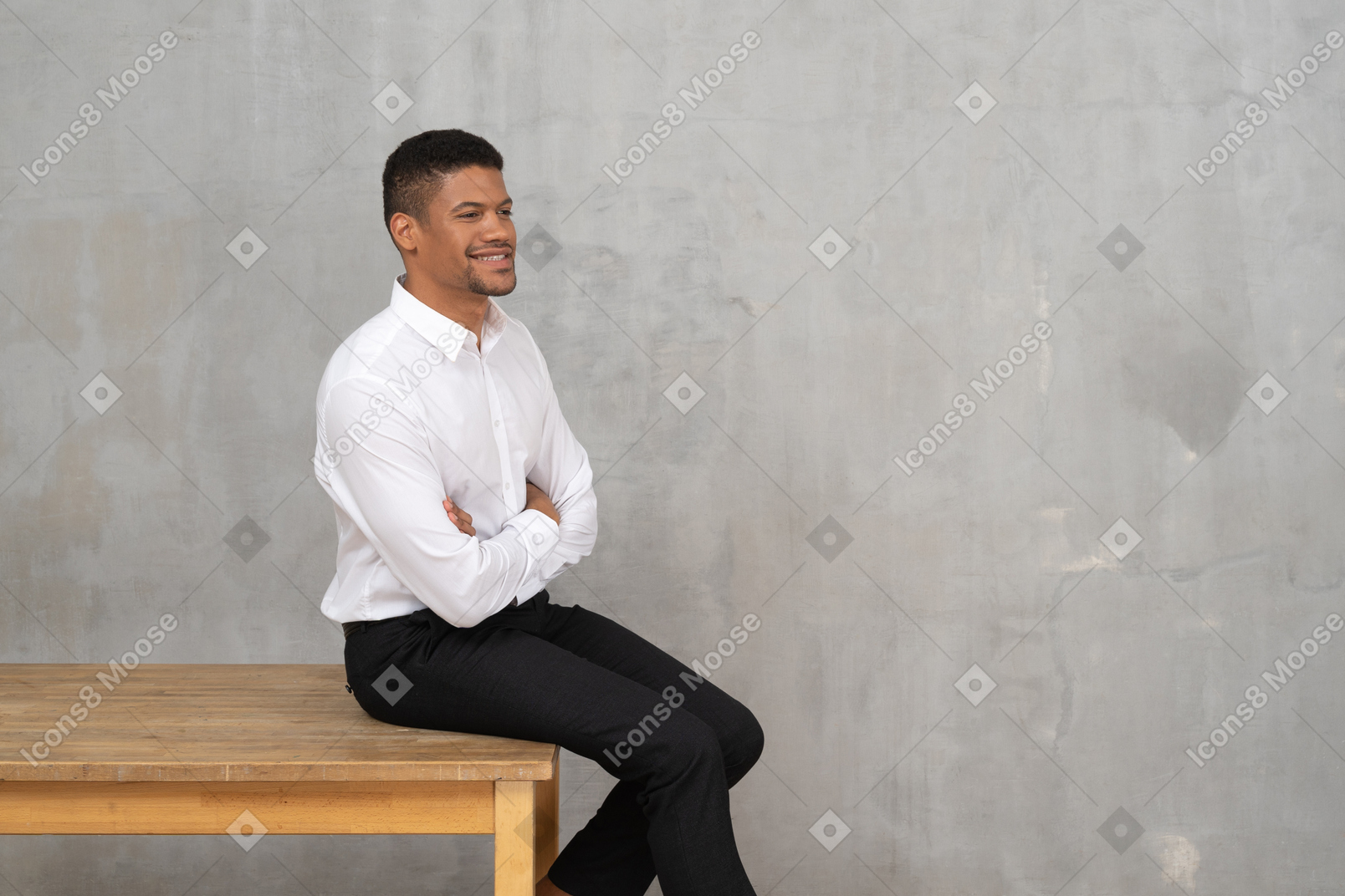 Homem sorridente em roupas de escritório, sentado em uma mesa com os braços cruzados