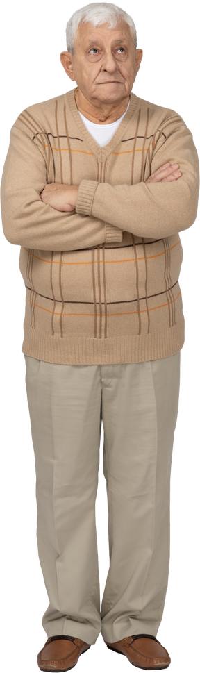 Vista frontal de un anciano con ropa informal de pie con los brazos cruzados y mirando hacia arriba