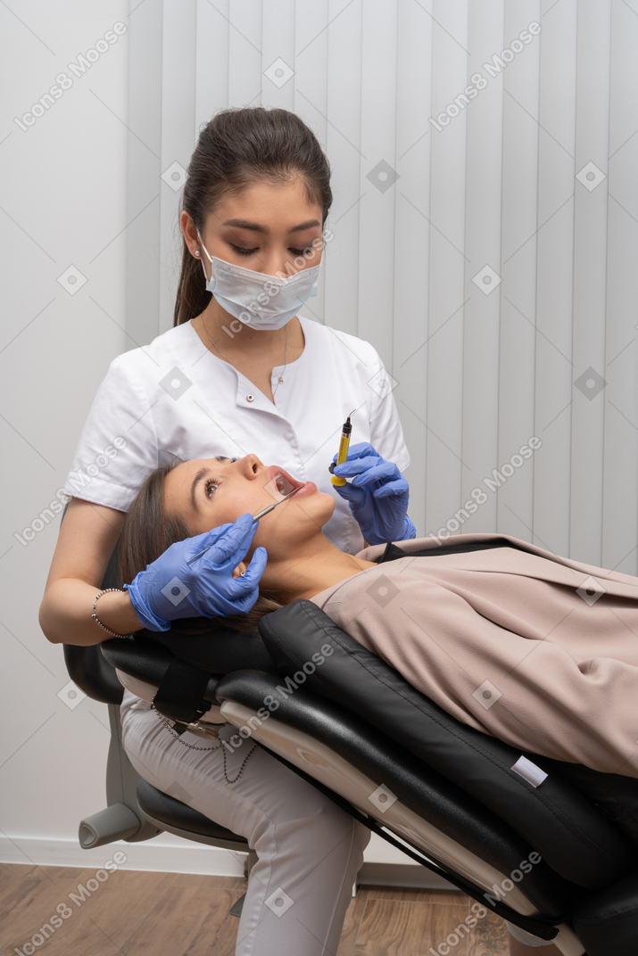 Dentista com máscara e luvas de látex injetando em sua paciente