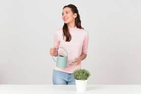 Attraente giovane donna innaffiando una pianta d'appartamento