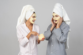 Deux, jeunes filles, cheveux, enveloppé dans, serviettes, appliquer, crème, masques, visage