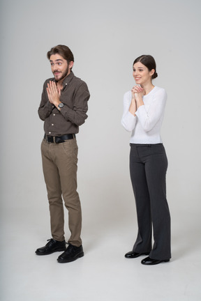Трехчетвертный вид довольной молодой пары в офисной одежде, держащейся за руки