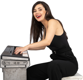 Vista laterale di una giovane donna sorridente seduta in abito nero mentre suona il pianoforte