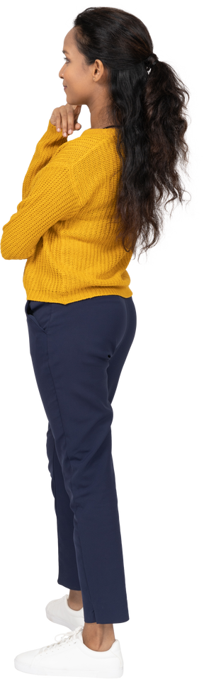 Vista lateral de una niña en ropa casual tocando la barbilla con los dedos y mirando hacia arriba