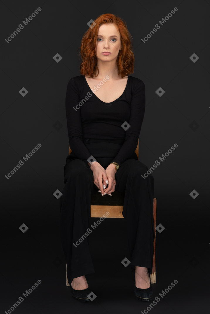 Sexy young woman sitting on the wooden chair and looking to the camera