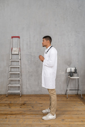 Side view of a young doctor standing in a room with ladder and chair explaining something