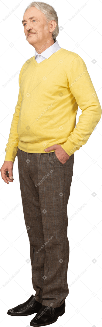 Vista di tre quarti di un vecchio scontento che indossa un maglione giallo e mette la mano in tasca e guarda da parte