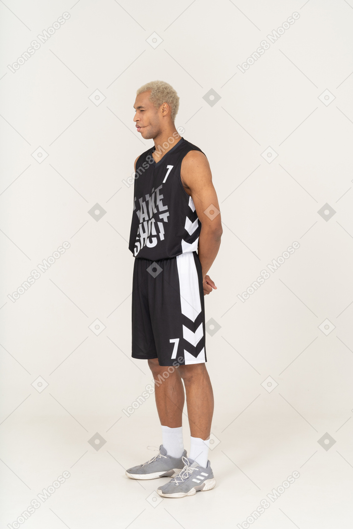Vista de três quartos de um jovem jogador de basquete, mordendo os lábios e de mãos dadas atrás
