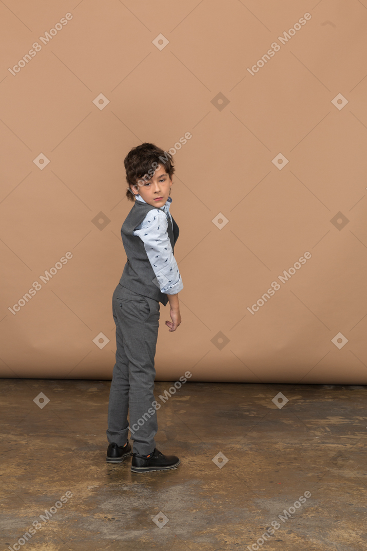 Vista lateral de un niño con traje gris mirando a la cámara