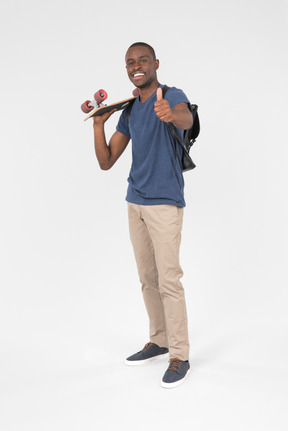 Male tourist holding skateboard and showing thumb up