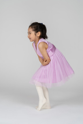 一个穿着芭蕾舞短裙的小女孩抱着肚子向前弯腰的侧视图