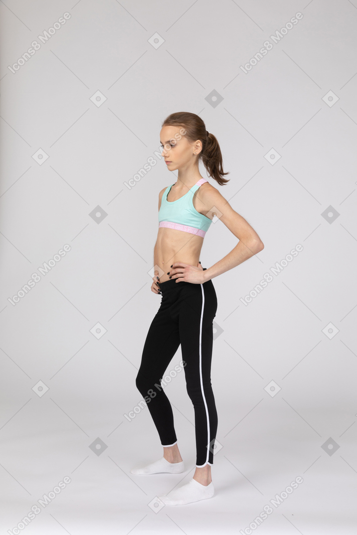 Вид в три четверти девушки-подростка в спортивной одежде, положившей руки на бедра
