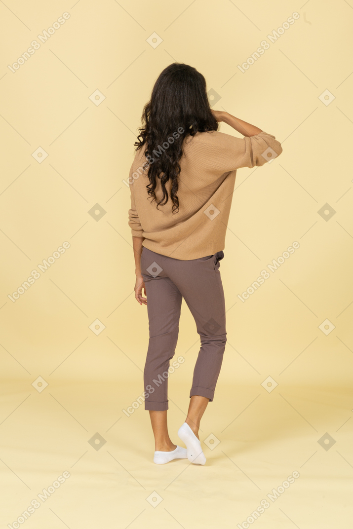 Three-quarter back view of a dark-skinned young female making a phone call gesture