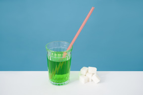 Стакан с зеленой жидкостью и кубиками сахара