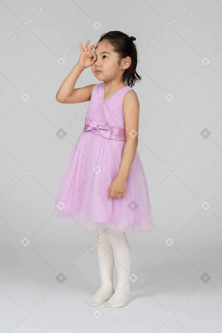 Kleines mädchen in rosafarbenem kleid, das durch ein okay-schild schaut