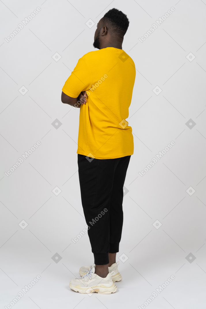 Three-quarter back view of a young dark-skinned man in yellow t-shirt crossing arms
