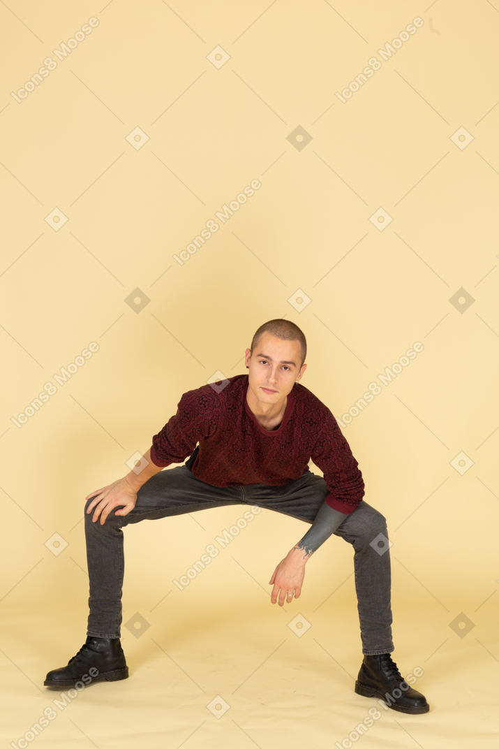 Вид спереди сидящего на корточках молодого человека в красном пуловере